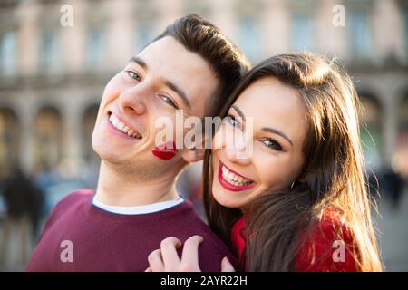 Junge lächelnde Paare Portrait, der Mann hat ein Lippenstiftkuss-Zeichen auf seiner Wange Stockfoto