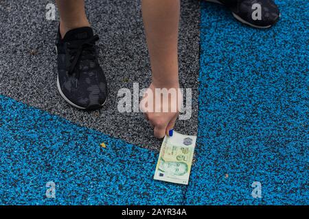 Hand nimmt eine 5 Dollar teure grüne Singapur-Note auf dem Boden auf. Stockfoto