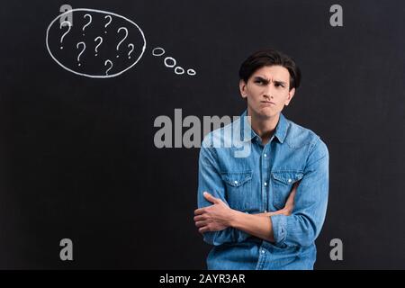 Nachdenklicher junger Mann mit Fragezeichen in Denkblase auf Tafel Stockfoto