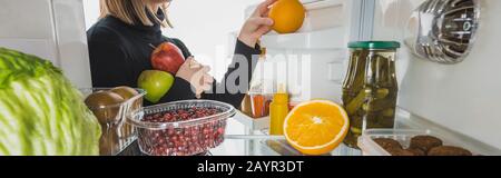 3/4-Ansicht des Mädchens, das frische Früchte aus dem Kühlschrank nimmt, isoliert auf weißem, Panoramabild, Stockbild Stockfoto