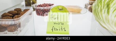 Panoramaaufnahme der Karte mit Eat More Fruits Schriftzug im Kühlschrank mit auf weißem, Stockbild isolierten Lebensmitteln Stockfoto