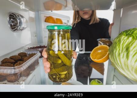 3/4-Ansicht der Frau, die mit Pickeln aus dem Kühlschrankregal weit in die weiße, Stock-Abbildung einzieht Stockfoto