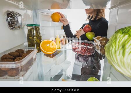 3/4-Ansicht der Frau, die reife Früchte aus dem Kühlschrank nimmt, mit auf weißem, Stockbild isoliertem Essen Stockfoto