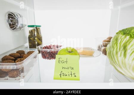 Karte mit Eat More Fruits Schriftzug im Kühlschrankregal mit auf weißem, Stockbild isolierten Lebensmitteln Stockfoto