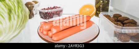 Panoramaaufnahme von Würstchen, Schnürsenkeln mit Kohl und Früchten im Kühlschrank isoliert auf weißem, Stockbild Stockfoto