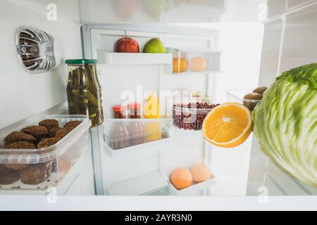 Schnürsenkel mit reifen Früchten und Kohl im Kühlschrank mit offener Tür isoliert auf weißem, Stockbild Stockfoto