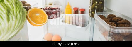 Panoramaaufnahme frischer Früchte mit Kohlschnitzeln und Soßen im Kühlschrank mit offener Tür, isoliert auf weißem Stockbild Stockfoto