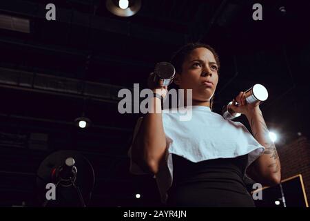 Niedriger Blickwinkel auf das training der afroamerikanischen Frau mit Hanteln im Fitnessstudio Stockfoto