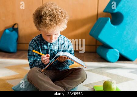 Intelligentes Kind, das auf das Notebook blickt und den Stift hält Stockfoto