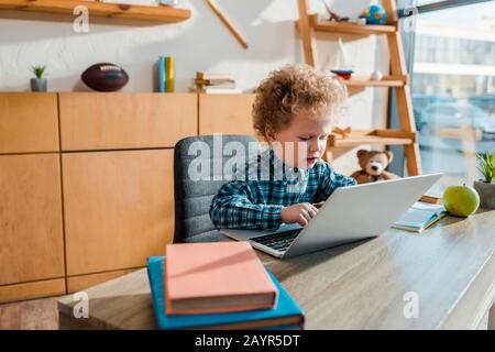 Selektive Fokussierung der lockigen Eingabe von Kindern auf Laptops in der Nähe von Büchern Stockfoto