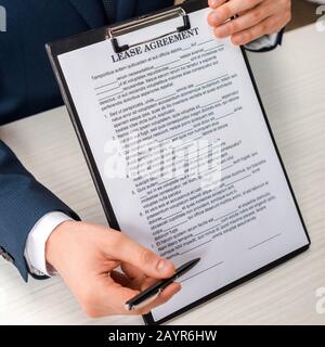 Beschnittener Blick auf die Zwischenablage des Geschäftsmannes mit Lease Agreement Schriftzug und Stift Stockfoto
