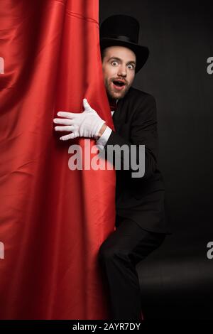 Überraschter Zauberer im Anzug und Hut im Zirkus mit roten Vorhängen Stockfoto