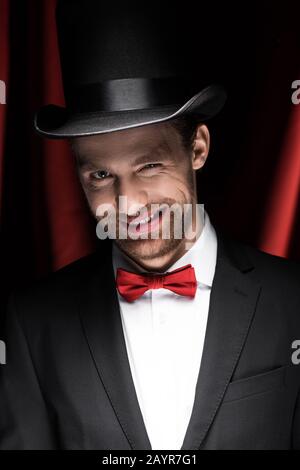 Lächelnder Zauberer winkelt im Zirkus mit roten Vorhängen Stockfoto