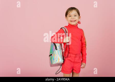 Ein süßes kleines Mädchen mit einem Rucksack auf der Schulter geht in die erste Klasse und freut sich. Das Konzept des Schulrückens. Vorlage für Ihre Werbung für Schulprodukte und 1. September. Stockfoto