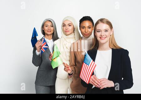 Attraktive multikulturelle Geschäftsfrauen mit Flaggen verschiedener Länder isoliert auf Weiß Stockfoto