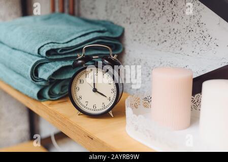 Massagezeit analoge schwarze Uhr auf einem Regal mit blauen Handtüchern und Wachskerzen. Das Konzept der Massageartikel. Stockfoto