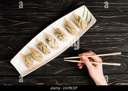 3/4-Ansicht der Frau, die köstliche chinesische gekochte Knödel mit Essstäbchen am schwarzen Holztisch isst Stockfoto