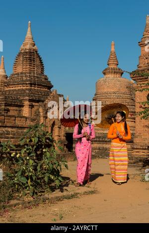 Ein Modellschießen mit zwei jungen Frauen in traditionellen Kleidungs- und Sonnenschirmen in einem kleinen Tempelkomplex in Bagan, Myanmar. Stockfoto