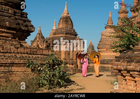 Ein Modellschießen mit zwei jungen Frauen in traditionellen Kleidungs- und Sonnenschirmen in einem kleinen Tempelkomplex in Bagan, Myanmar. Stockfoto