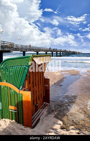 Sandstrand und traditioneller Strandstuhl aus Holz auf der Insel Rügen, Norddeutschland. Im Hintergrund die Seebrücke. Stockfoto