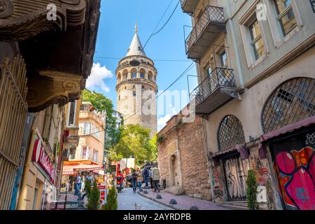 Touristen wandern durch die engen, hügeligen Straßen vorbei an Geschäften unter dem historischen Galata-Turm im Karakoy-Viertel in Istanbul, Türkei. Stockfoto