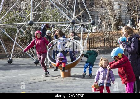 Kinder und Eltern genießen einen milden Wintertag auf einem Spielplatz im Prospect Park, Brooklyn, New York. Stockfoto