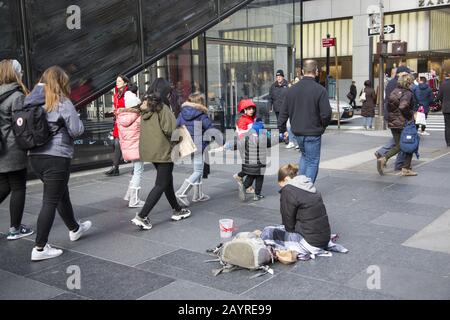 Obdachlose Frau bittet demütig um Spenden auf dem breiten Bürgersteig an der 5th Avenue in Midtown Manhattan, New York City. Stockfoto