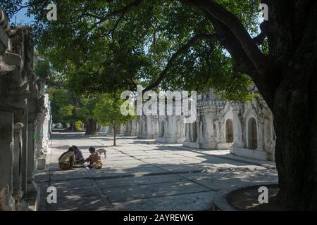 Lokale Frauen und ein Hund an den Stupas-Reihen, die jeweils eine der 729 Platten enthalten, die mit den buddhistischen Lehren in der Kuthodaw-Pagode auf Mandalay eingraviert sind Stockfoto