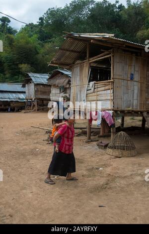 Eine lokale Frau geht vor traditionellen Häusern auf Stelzen aus Bambus im Ban Muangkeo Village, einem Kulturerbe-Dorf am Mekong Stockfoto