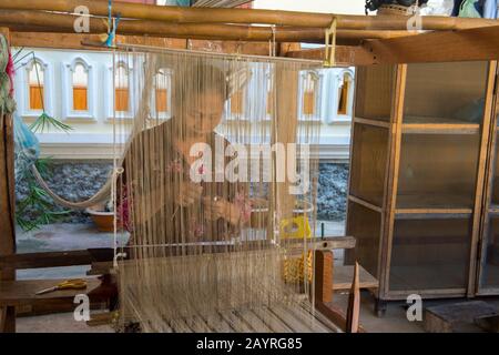 Eine Frau auf einem Webstuhl webt in einer Werkstatt in Ban Xang Khong, einem Dorf in der Nähe von Luang Prabang in Zentral-Laos, die für bekannt ist, Seide- und Baumwollstoffe Stockfoto