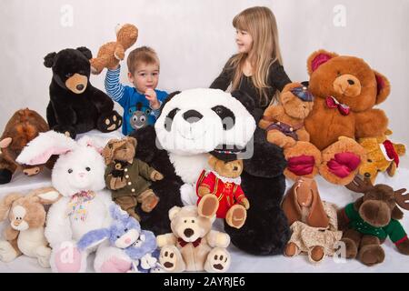 Sammlung von ausgestopften Tieren mit 2 jährigen Jungen hält seinen Teddy und seine 5-jährige Schwester Stockfoto