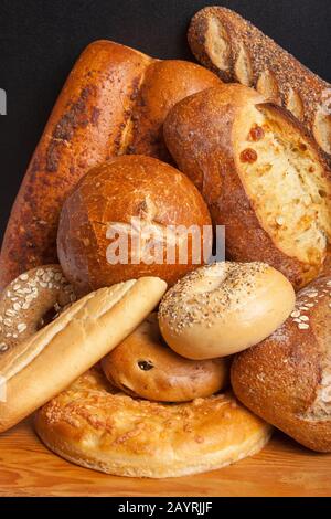 Verschiedene hausgemachte Brotsorten auf einer rustikalen Holzschneideplatte, einschließlich Sauerteigbrotschüssel, Sauerteig Laib, drei Saat Laib, drei Käse Laib, französisch Stockfoto