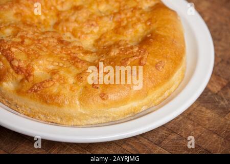 Ganze Laibe mit Focaccia-Brot auf einer weißen Keramikplatte auf einem rustikalen Holztisch Stockfoto