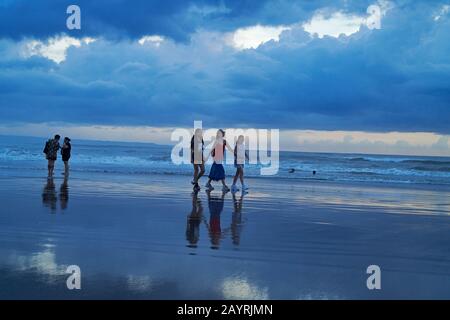 Mutter und ihre beiden Töchter gehen bei Sonnenuntergang Hand in Hand am Strand in Bali entlang Stockfoto