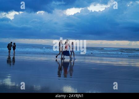 Mutter und ihre beiden Töchter gehen bei Sonnenuntergang Hand in Hand am Strand in Bali entlang Stockfoto