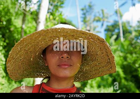 Nahaufnahme des Porträts einer asiatischen Frau, die bei strahlendem Sonnenschein einen großen Strohhut trägt, um sich vor der heißen Sonne zu schützen Stockfoto