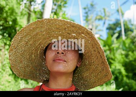 Nahaufnahme des Porträts einer asiatischen Frau, die bei strahlendem Sonnenschein einen großen Strohhut trägt, um sich vor der heißen Sonne zu schützen Stockfoto