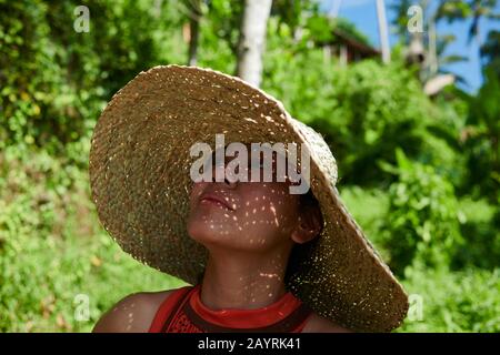 Nahaufnahme des Porträts einer asiatischen Frau, die bei strahlendem Sonnenschein einen großen Strohhut trägt, um sich vor der heißen Sonne zu schützen Stockfoto