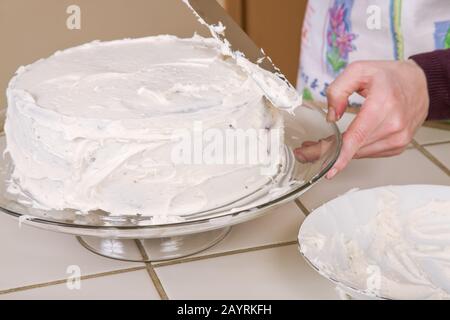Frau, die auf einem gläsernen Kuchenständer einen Karottenkuchen mit Sahne aufschäumt Stockfoto