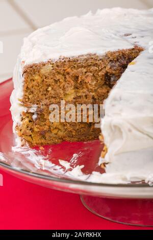 Ganze Karottenkuchen mit einer Scheibe entfernt, die auf einem gläsernen Kuchenständer ruht Stockfoto