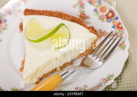 Scheibe aus Kalkkuchen, oben mit einer verdrehten Kalkscheibe, die auf einer china-platte auf einem Tischtuch mit Blumenmuster aufliegt Stockfoto