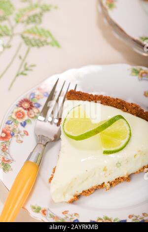 Scheibe aus Kalkkuchen, oben mit einer verdrehten Kalkscheibe, die auf einer china-platte auf einem Tischtuch mit Blumenmuster aufliegt Stockfoto