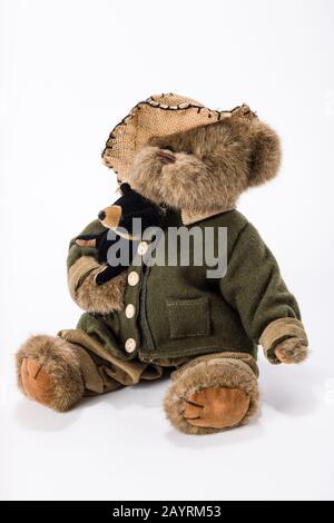 Gestopfter Teddybär, der eine Jacke, eine Hose und einen Hut trägt und seinen eigenen Teddybären hält Stockfoto