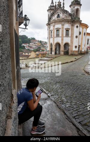 Ouro PRETO, MINAS GERAIS, BRASILIEN - 22. DEZEMBER 2019: Eine nicht identifizierte Frau verwendet ihr Telefon in Largo do Rosario, Ouro Preto - Brasilien. Ouro Preto war de Stockfoto