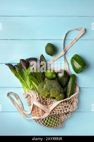 Grünes Gemüse und Obst in einem wiederverwendbaren Saitenbeutel auf hellblauem Hintergrund. Ökologisches Konzept, Draufsicht Stockfoto