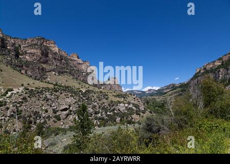 Die schöne Landschaft des Ten Sleep Canyon auf der Route 16 in Wyoming mit hohen Felsklippen, grünen Pinsel und Bäumen und einem klaren blauen Himmel. Stockfoto