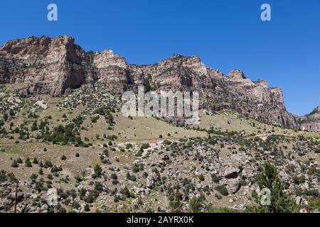 Die schöne Landschaft des Ten Sleep Canyon auf der Route 16 in Wyoming mit hohen Felsklippen, grünen Pinsel und Bäumen und einem klaren blauen Himmel. Stockfoto