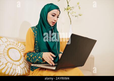 Muslimische Unternehmerinnen, die Ohrhörer tragen, wenn sie Videokonferenzen mit Geschäftspartnern oder Kunden führen, um das Projekt zu besprechen Stockfoto