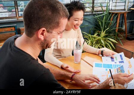 Glückliche multiethnische Jungunternehmer, die Berichte diskutieren und an der Marketingstrategie arbeiten Stockfoto