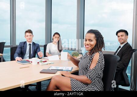 Positive lächelnde Black Business Lady, die mit Kollegen zusammenspricht und Finanzberichte und neue Entwicklungsstrategie diskutiert Stockfoto
